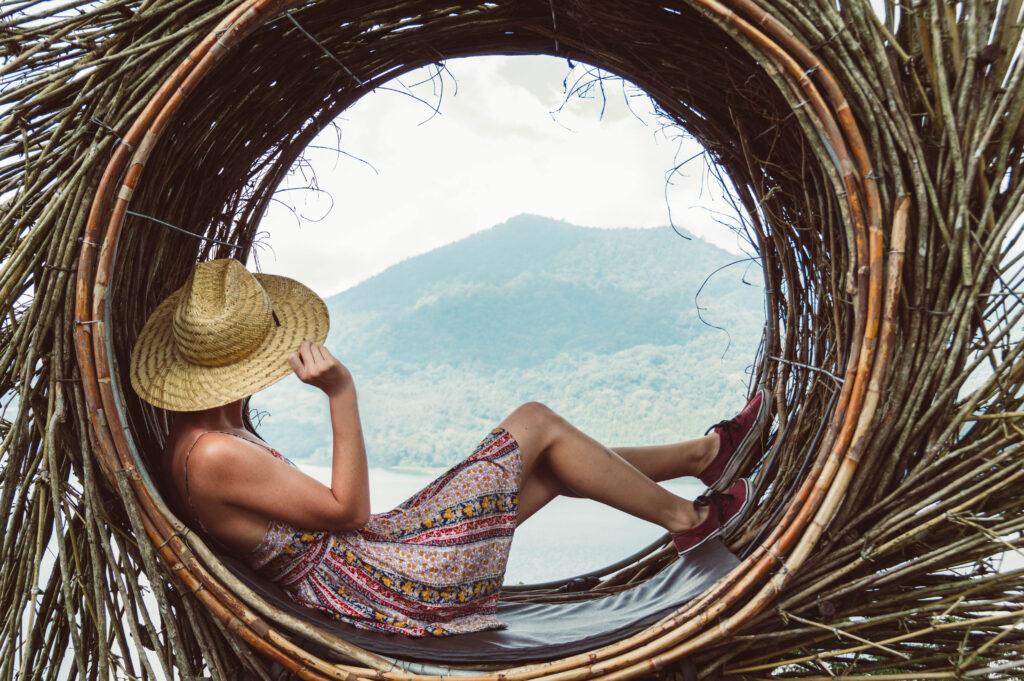 Tips for sustainable travel: Just enjoy yourself, like this young woman lying in a round lounger enjoying the view. She is wearing a summer dress and a stubble hat