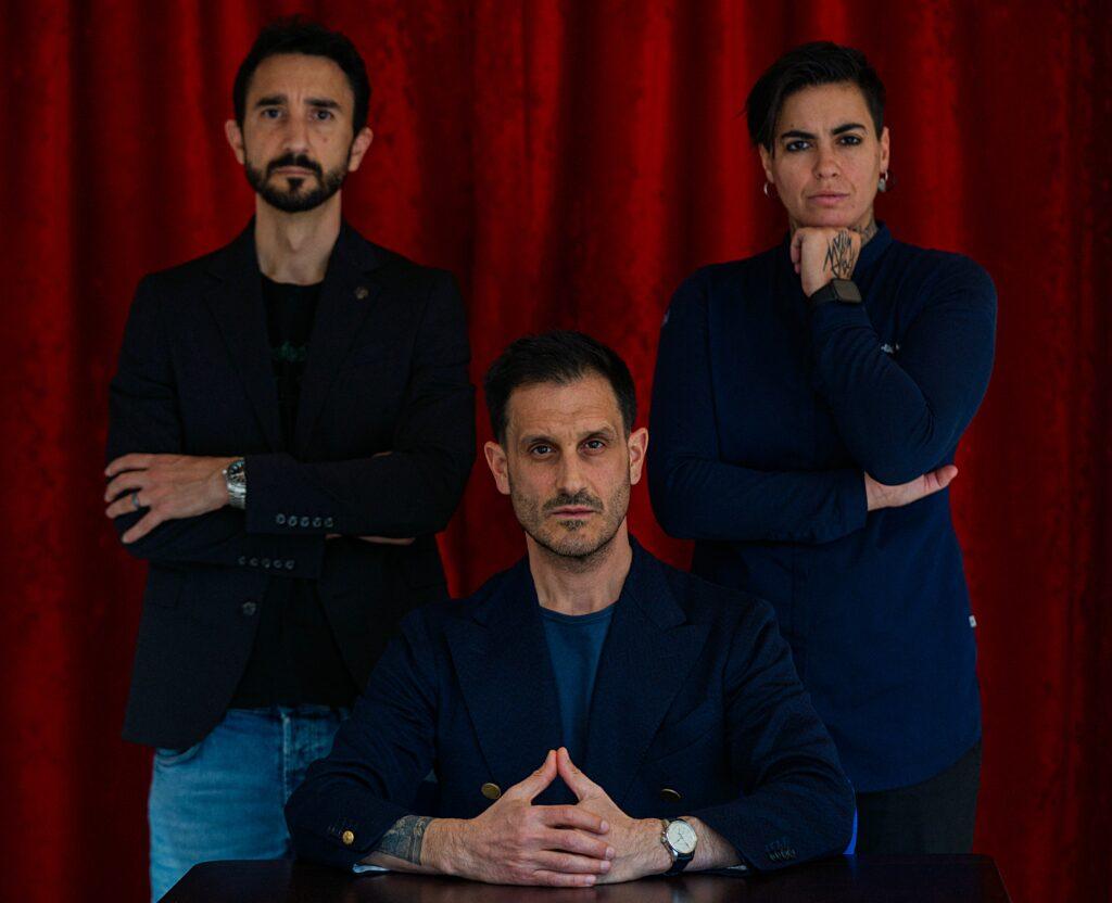 Alexander and Maximilian Sprögler pose in front of a curtain with vegan chef Aggeliki.