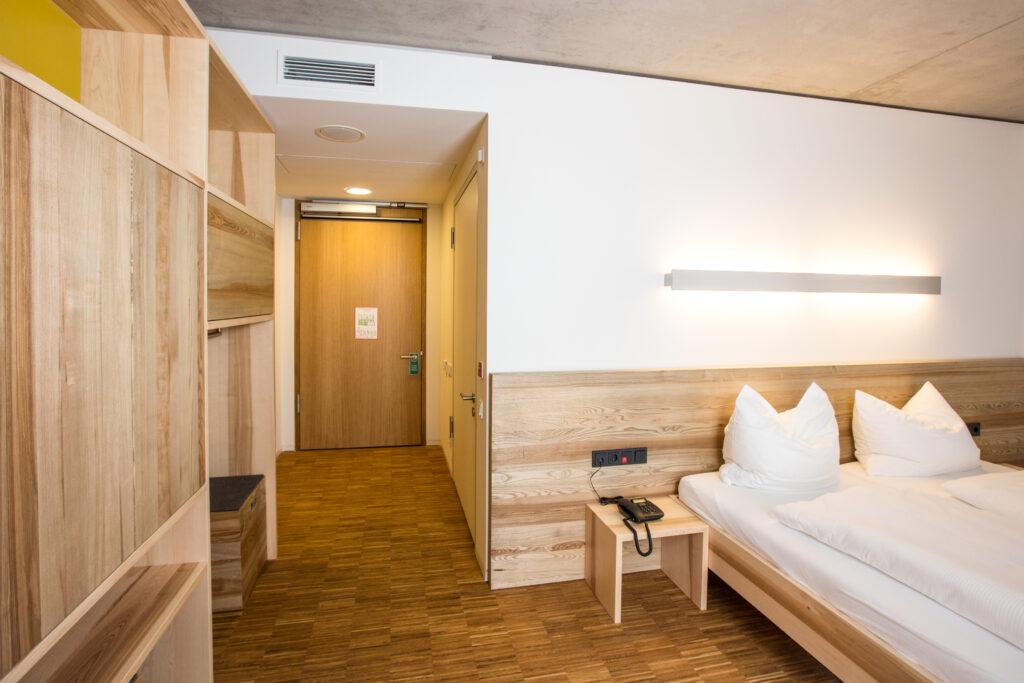 The hotel rooms feature sustainable wooden furniture. Pictured are a bed, a wardrobe, and a hallway.