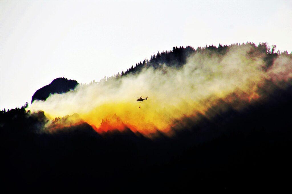 A forest fire with a helicopter flying in front of the smoke cloud.