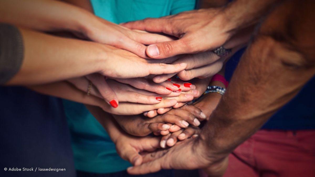 Mehrere Hände liegen übereinander. Repräsentiert sind verschiedene Hautfarben und unterschiedliche Ethnien und Geschlechter