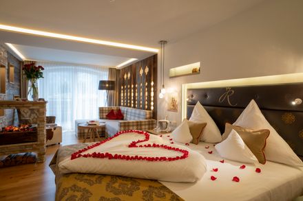 A hotel bed adorned with rose petals arranged in the shape of a heart.