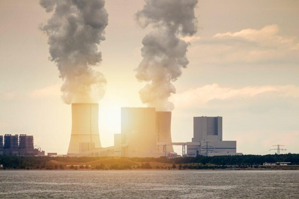 Coal-fired power plant with two large cooling towers spewing thick smoke into a sunset sky.