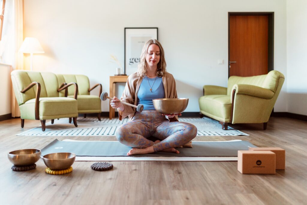 Karen from Hotel Okelmanns is sitting cross-legged on the floor with a singing bowl. A sustainable and mindful lifestyle.