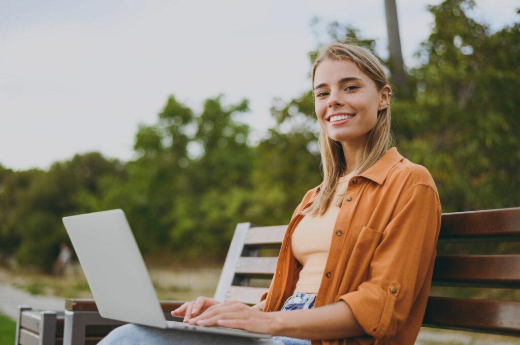 A young woman in nature with a laptop, discussing sustainable travel planning.