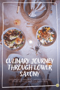 Plates of diverse, colorful dishes on a rustic table with cutlery and a napkin, featuring text "Culinary Journey Through Lower Saxony." Cozy and inviting at the Hotel Okelmann's.