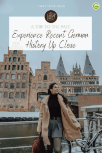 Woman in cozy winter attire stands near a river with historic buildings of the German town Lübeck in the background. The scene conveys a sense of exploration and nostalgia.