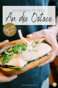 Nahaufnahme eines Sandwichs, das mit beiden Händen gehalten wird und mit weißem Fisch, Salat und Kräutern gefüllt ist. Der Text darüber lautet: „Kulinarische Reise an der Ostsee“.