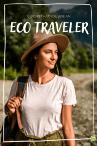 Woman in a hat and casual attire smiles while holding a bag. Background features lush greenery and mountains. Text reads "15 Signs That You Are an Eco Traveler."