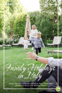 Family playing in the lush garden of the sustainable hotel Relais del Maro; a woman and two children running joyfully toward the camera. Text overlay: "Family Holidays in Italy." Summer vibe.
