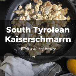 A skillet of golden Kaiserschmarrn dusted with powdered sugar. Nearby are a lemon, grater, and utensils on a cloth. Text reads "South Tyrolean Kaiserschmarrn."
