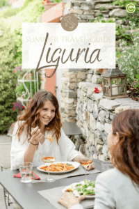 Outdoor dining scene in the Relais del Maro Albergo Diffuso hotel in Liguria; two women enjoy pasta and wine near a stone wall. The mood is relaxed and joyful, with lush greenery around.